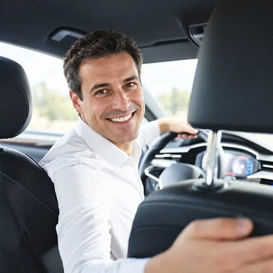 Un homme assis au volant d’une voiture se retourne en souriant vers l’arrière.