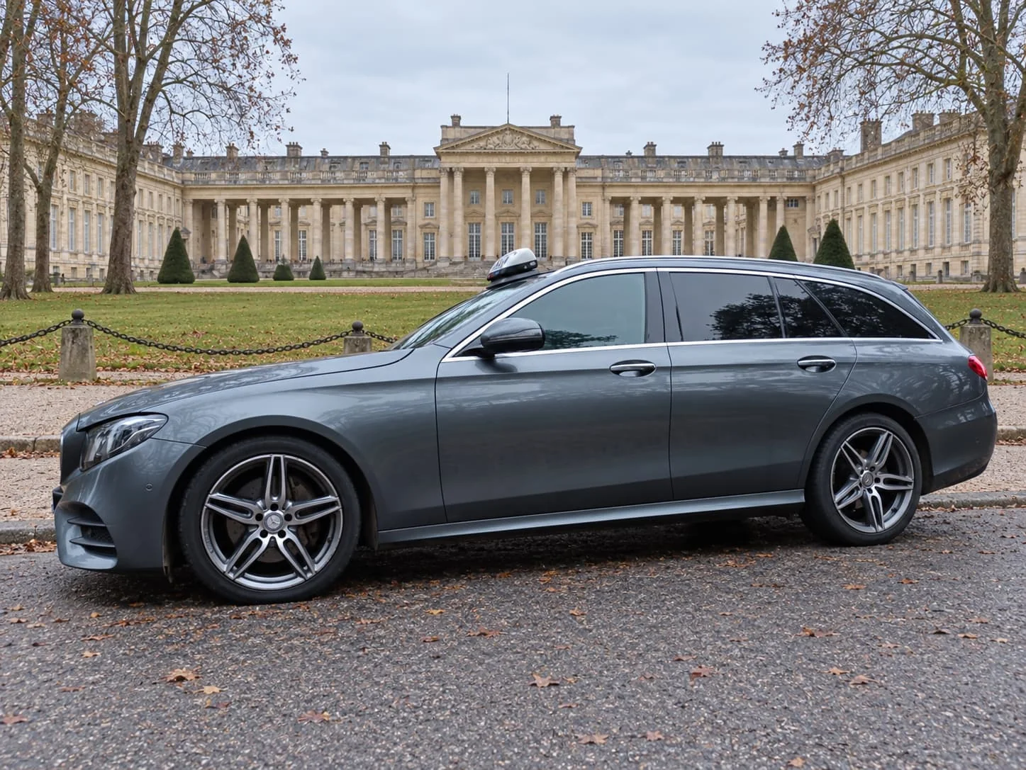 Taxi Mercedes break gris stationné devant un château entouré d’arbres.