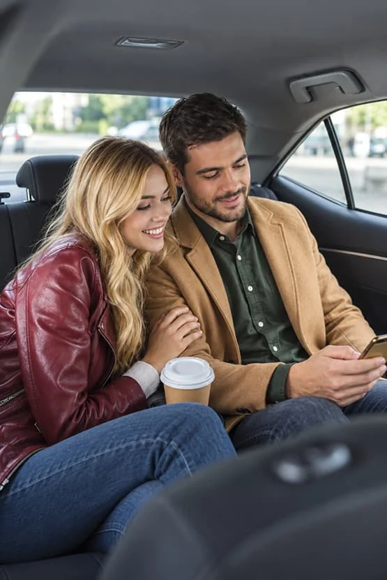 Un couple assis à l’arrière d’une voiture regarde un smartphone.
